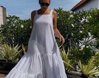 Könnte beinhalten: Ein weißes Maxikleid mit quadratischem Ausschnitt und dünnen Trägern. Das Kleid hat einen Stufenrock und ist aus einem leichten Stoff gefertigt.