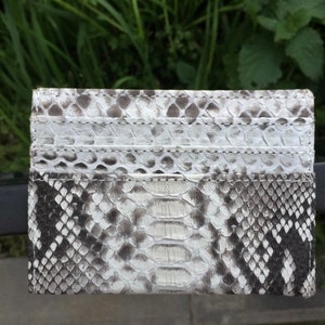 May include: A white and gray snakeskin card holder with a textured pattern. The card holder has multiple slots for cards.