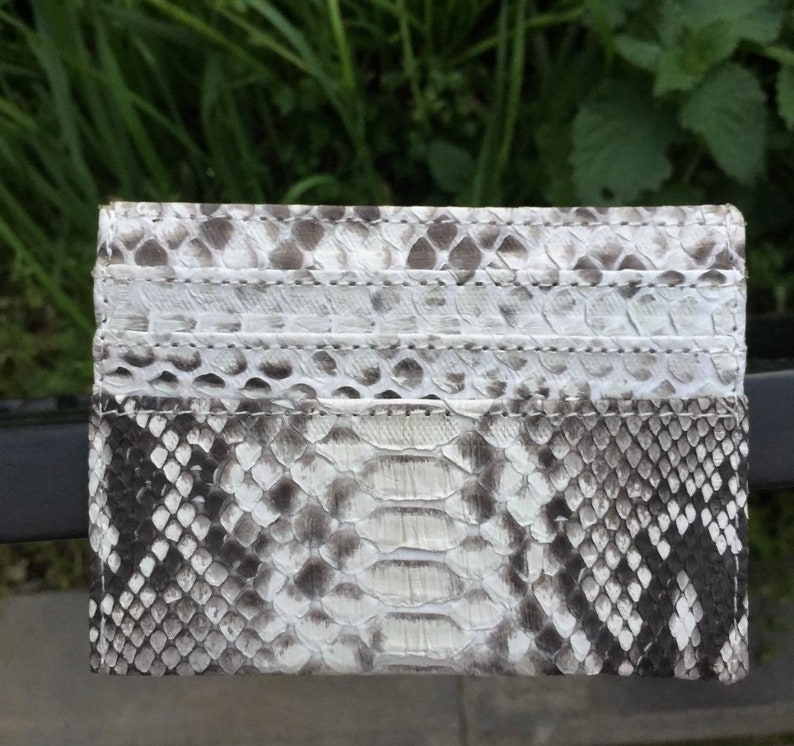 May include: A white and gray snakeskin card holder with a textured pattern. The card holder has multiple slots for cards.
