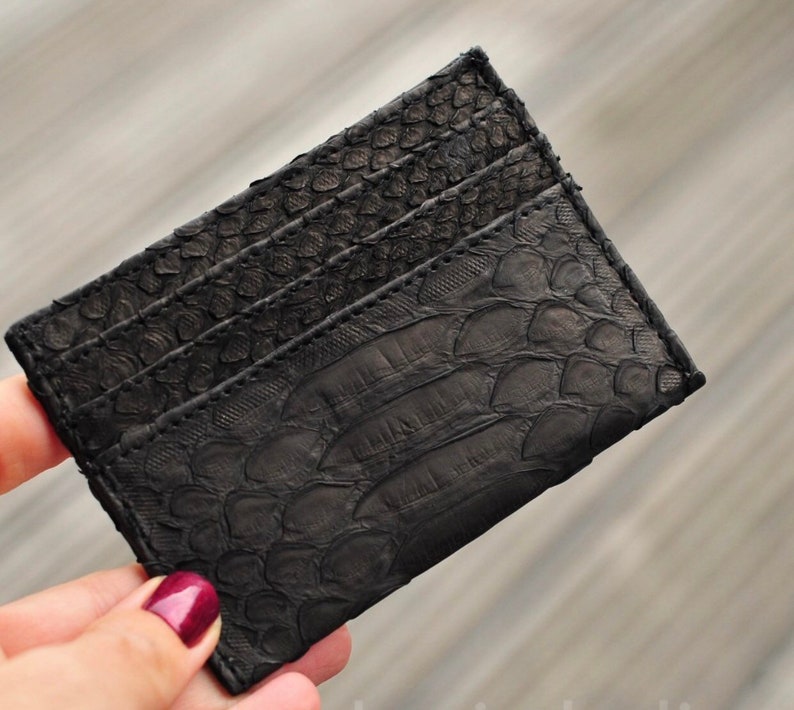 Puede incluir: Un tarjetero de cuero negro con un patr&oacute;n texturizado y estampado que se asemeja a escamas. El tarjetero tiene m&uacute;ltiples ranuras para tarjetas.