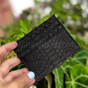 Puede incluir: Porta tarjetas de cuero negro con un patr&oacute;n en relieve de piel de serpiente.