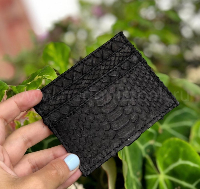 Puede incluir: Porta tarjetas de cuero negro con un patr&oacute;n en relieve de piel de serpiente.