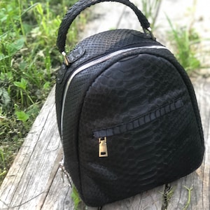 Könnte beinhalten: Ein schwarzer Lederrucksack mit Schlangenhautmuster. Der Rucksack hat einen Tragegriff oben und einen Reißverschluss.