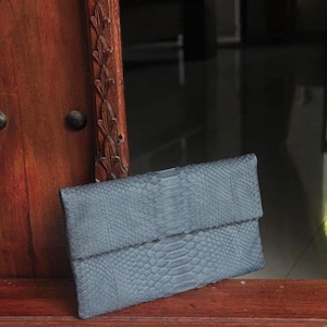 Może przedstawiać: Czarna skórzana kopertówka ze skóry węża z klapką.