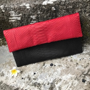 Può includere: Una pochette in pelle di serpente rossa e nera. Il lembo superiore è rosso e il fondo è nero.