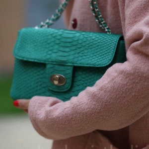 May include: A teal green snakeskin-textured handbag with a silver clasp and a chain strap.