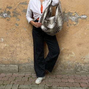 May include: A woman wearing a white button-down shirt, black pants, and white sneakers. She is holding a snakeskin handbag and wearing sunglasses.