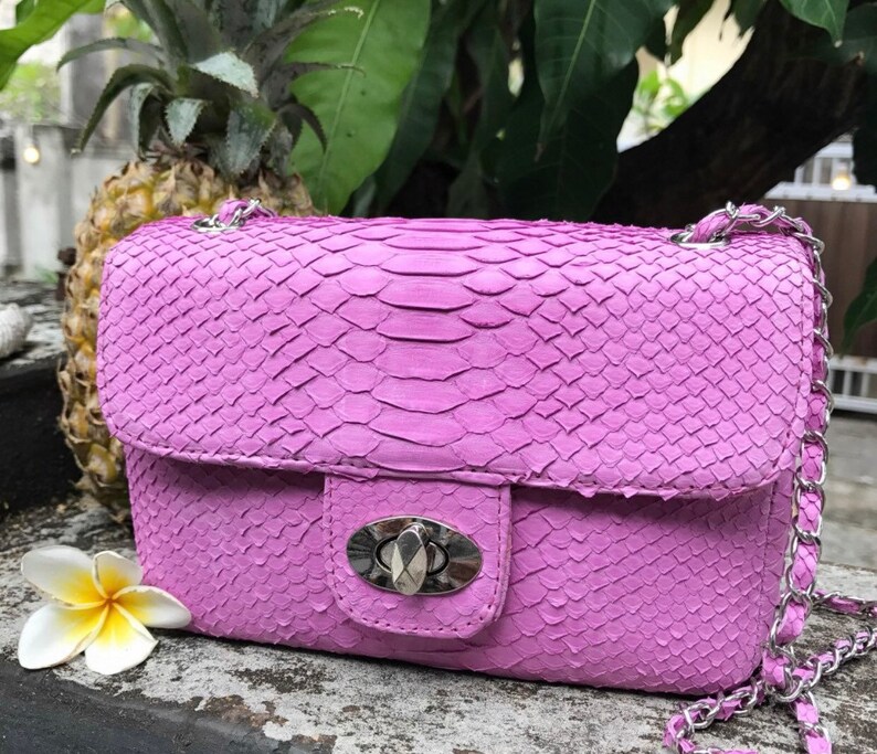 K&ouml;nnte beinhalten: Eine leuchtend pinkfarbene Schlangenlederschultertasche mit einer silbernen Kettenkette und einem silbernen Verschluss. Die Tasche hat eine strukturierte Oberfl&auml;che und einen Klappenverschluss.