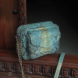 Può includere: Una piccola borsa a tracolla in pelle di serpente turchese e oro con una tracolla a catena dorata.