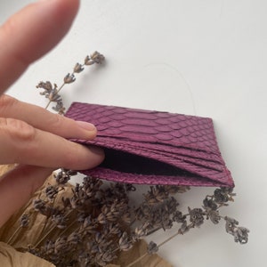 K&ouml;nnte beinhalten: Ein Kartenetui aus violettem Schlangenleder mit schwarzem Innenfutter. Das Kartenetui ist ge&ouml;ffnet und das Innere ist sichtbar.