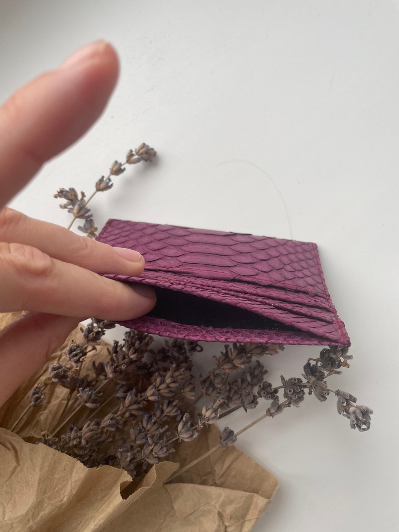 K&ouml;nnte beinhalten: Ein Kartenetui aus violettem Schlangenleder mit schwarzem Innenfutter. Das Kartenetui ist ge&ouml;ffnet und das Innere ist sichtbar.