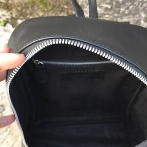 以下が含まれることがあります： シルバーのジッパーが付いた黒い革のバックパック。バッグの中は空です。