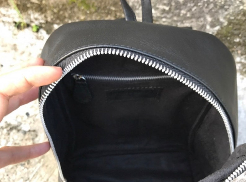 以下が含まれることがあります： シルバーのジッパーが付いた黒い革のバックパック。バッグの中は空です。