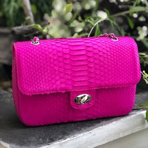 May include: A bright pink snakeskin shoulder bag with a silver chain strap and a silver clasp closure.