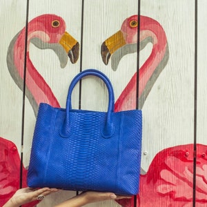 May include: A blue leather handbag with a textured snakeskin pattern. The bag has two top handles and a zipper closure.