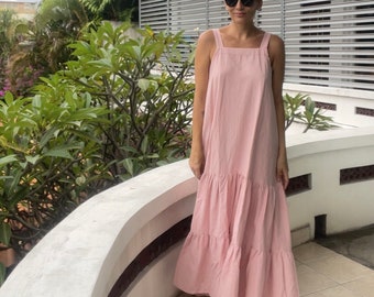 May include: A pink tiered maxi dress with thin straps. The dress is made of a lightweight fabric and has a relaxed fit.