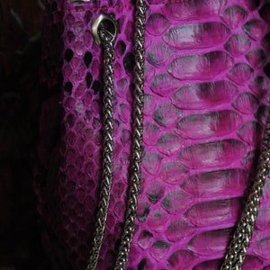 Op de afbeelding: Een close-up van een paarse slangenleren handtas met een zilveren kettingband.