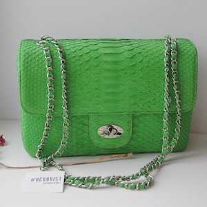 May include: A bright green snakeskin shoulder bag with a silver chain strap and a silver clasp. The bag has a #HEDONIST label attached to the strap.