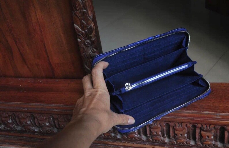 Op de afbeelding: Een blauwe portemonnee met rits met meerdere vakken en een zilveren rits.