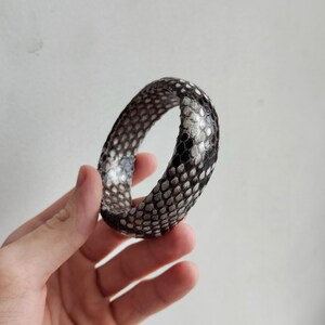 Może przedstawiać: Bransoletka ze skóry węża w kolorze czarnym i białym z fakturowanym wzorem.