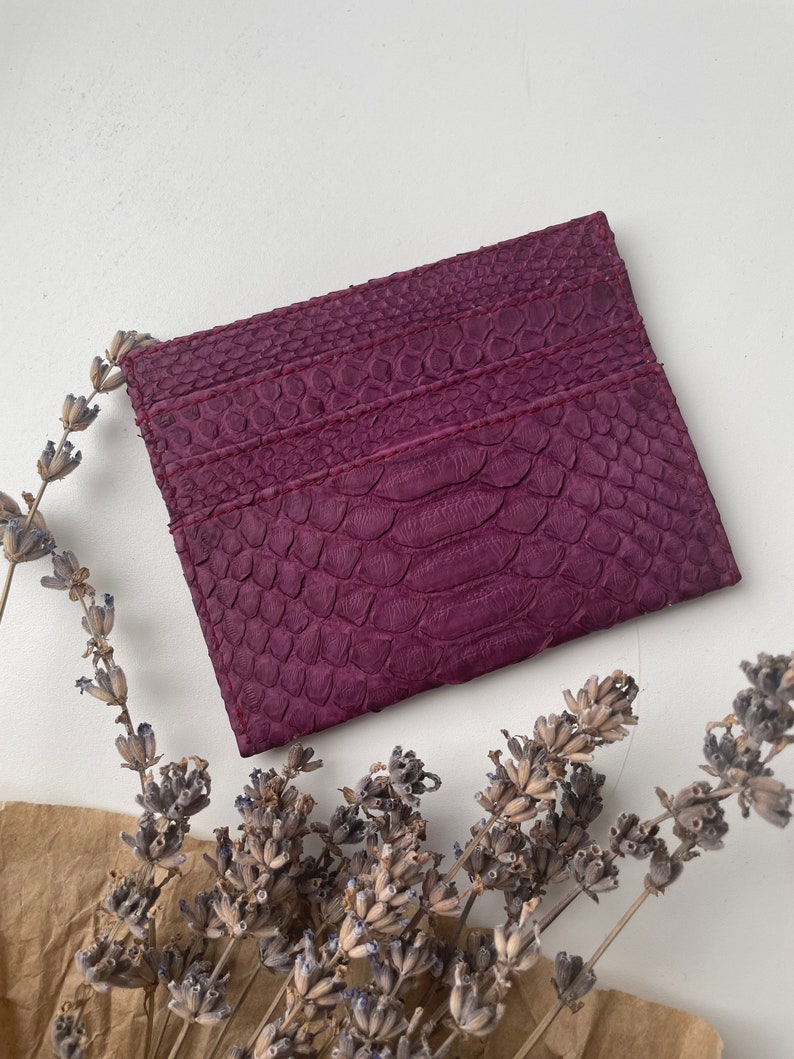 K&ouml;nnte beinhalten: Ein Kartenetui aus lila Leder mit Schlangenhautmuster. Das Kartenetui hat drei F&auml;cher f&uuml;r Karten.