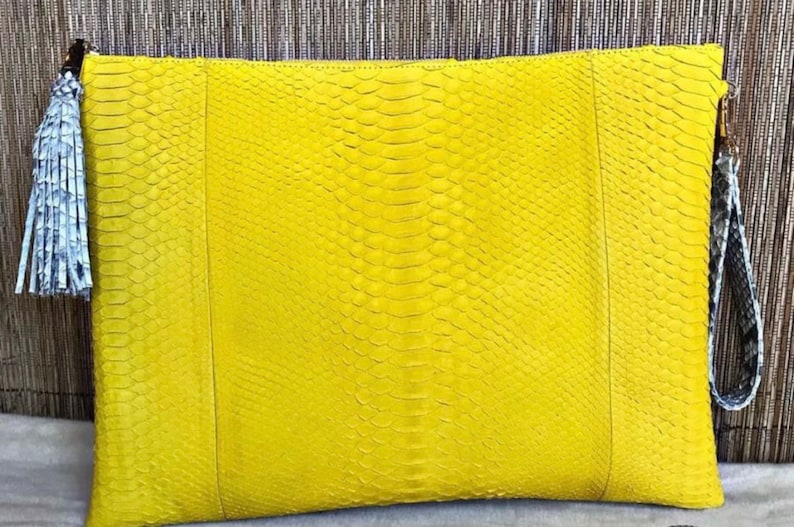 May include: A bright yellow clutch bag made of snakeskin with a gray and white tassel.