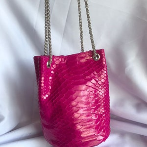 May include: A bright pink snakeskin bucket bag with a silver chain strap.