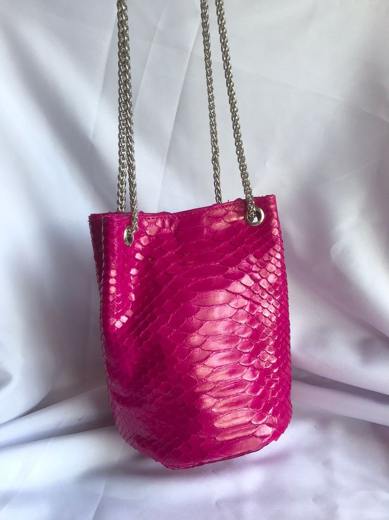 May include: A bright pink snakeskin bucket bag with a silver chain strap.