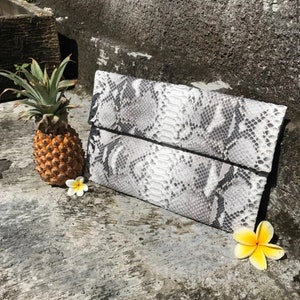 May include: A white and gray snakeskin clutch purse with a fold-over flap.