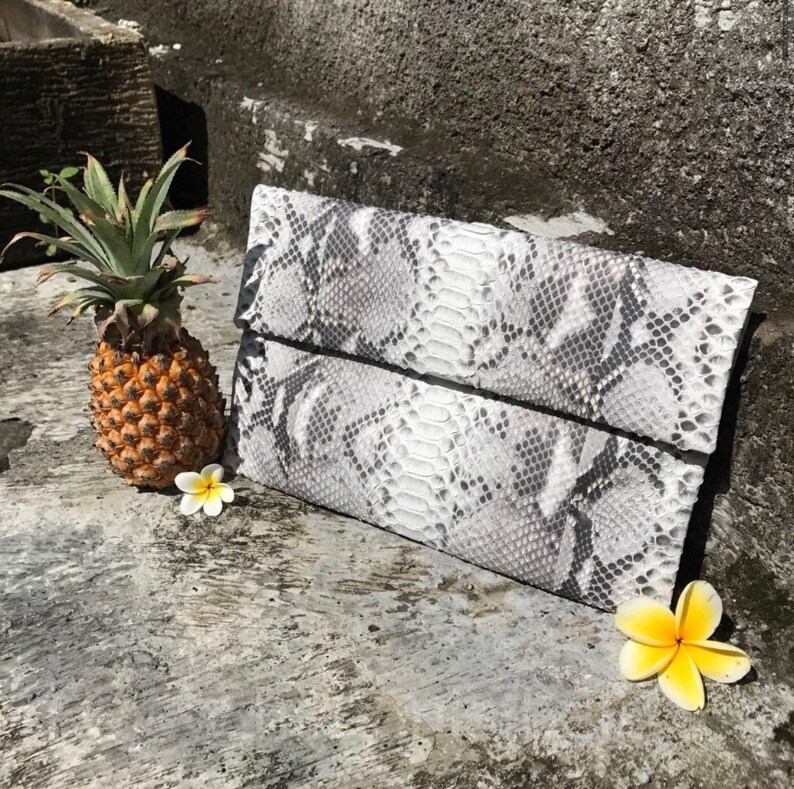 May include: A white and gray snakeskin clutch purse with a fold-over flap.