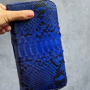 Op de afbeelding: Een blauwe en zwarte slangenleren portemonnee met een ritssluiting.