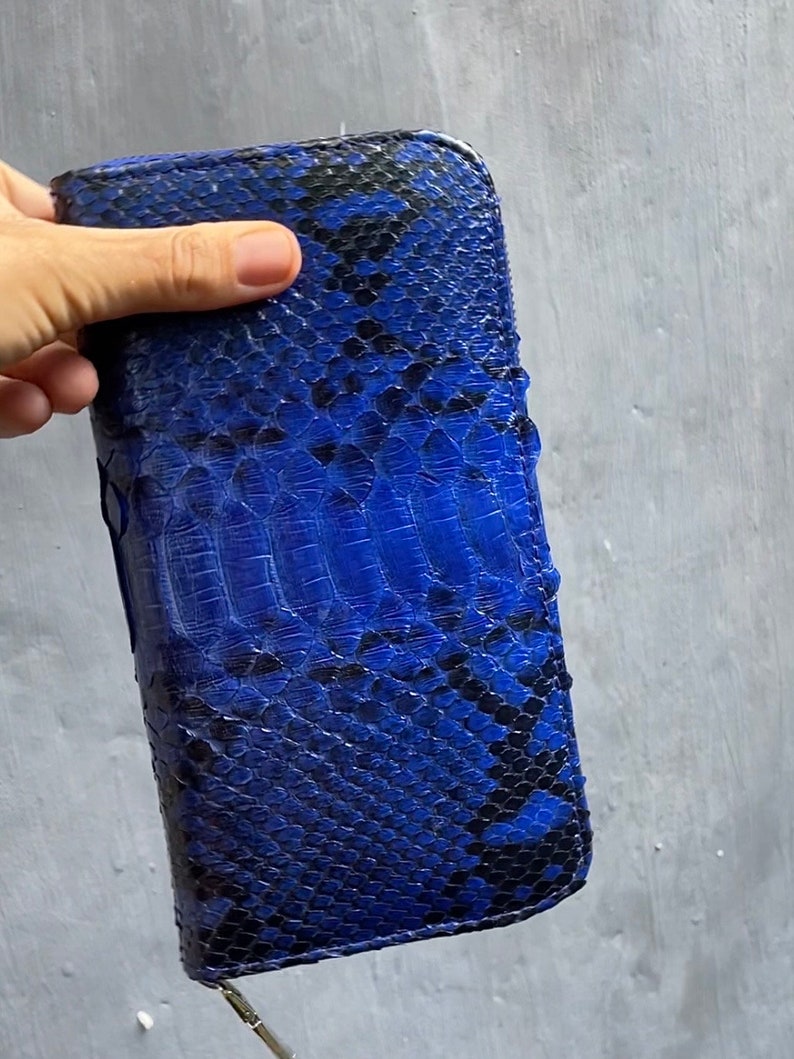 Op de afbeelding: Een blauwe en zwarte slangenleren portemonnee met een ritssluiting.