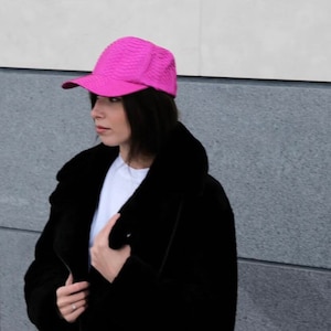 Può includere: Una donna indossa una giacca di pelliccia sintetica nera con un berretto da baseball rosa.