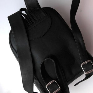 以下が含まれることがあります： 調節可能なストラップとシルバーのバックルが付いた黒い革のバックパック。バックパックはフラップクロージャーと前面に小さなポケットがあります。