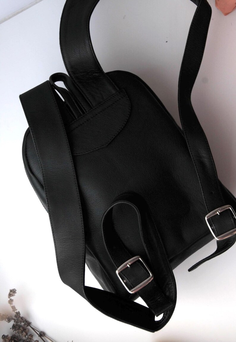 以下が含まれることがあります： 調節可能なストラップとシルバーのバックルが付いた黒い革のバックパック。バックパックはフラップクロージャーと前面に小さなポケットがあります。