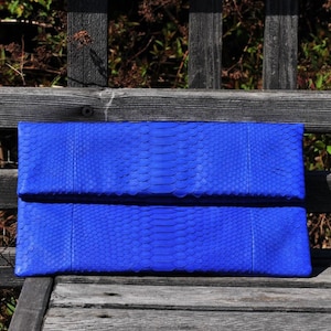 Pode incluir: Uma carteira de mão azul brilhante feita de pele de cobra. A carteira tem uma aba dobrável e uma superfície texturizada.