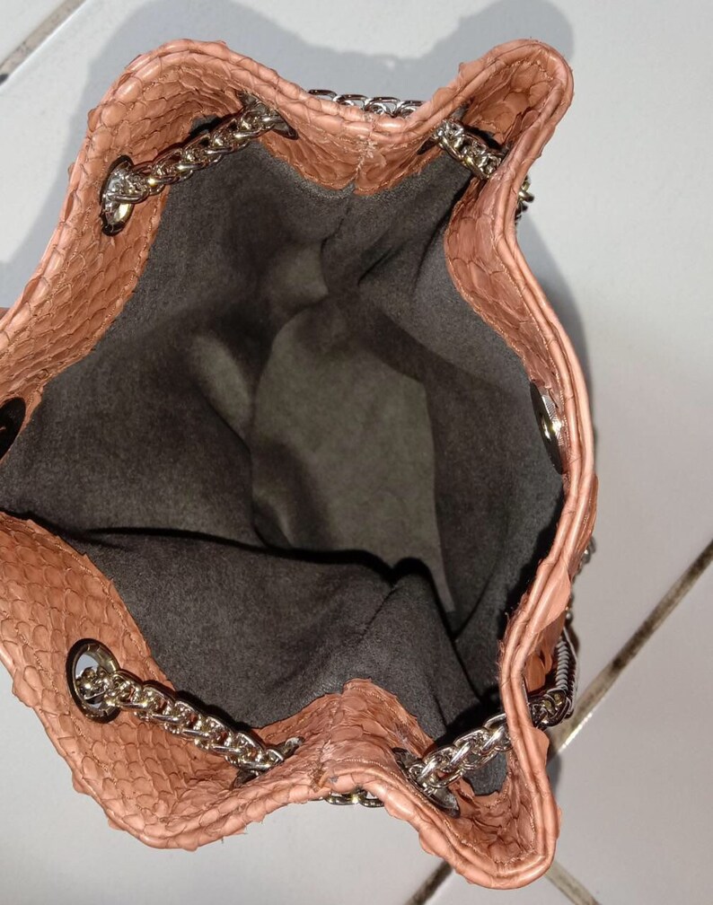May include: A light brown snakeskin bucket bag with a silver chain strap. The bag is open and the inside is lined with a dark grey fabric.