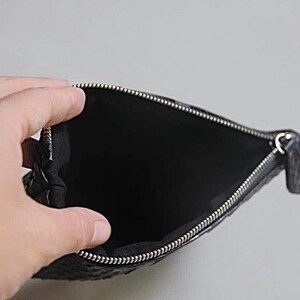 Może przedstawiać: Czarna sk&oacute;rzana kosmetyczka z srebrnym zamkiem błyskawicznym. Kosmetyczka jest otwarta i pusta.