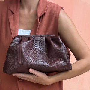 May include: A burgundy snakeskin clutch purse with a gathered design.