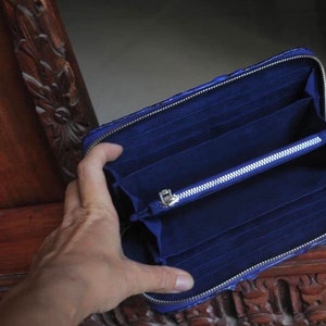 Op de afbeelding: Een blauwe leren portemonnee met een ritssluiting en meerdere kaartsleuven. De portemonnee is open en de binnenkant is gevoerd met een donkerblauwe stof.