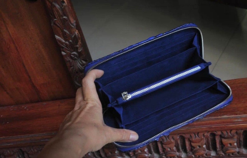 Op de afbeelding: Een blauwe leren portemonnee met een ritssluiting en meerdere kaartsleuven. De portemonnee is open en de binnenkant is gevoerd met een donkerblauwe stof.