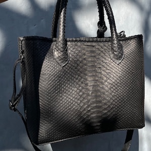 May include: A black leather tote bag with a snakeskin pattern and a long shoulder strap.