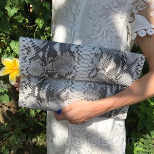 May include: A gray and white snakeskin clutch purse with a fold-over flap.