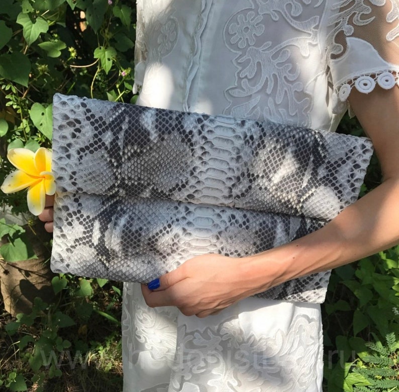 May include: A gray and white snakeskin clutch purse with a fold-over flap.