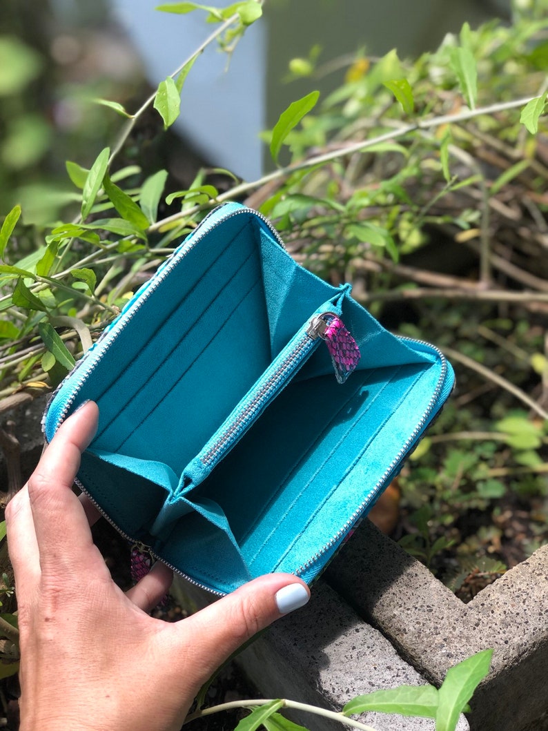 以下が含まれることがあります： ジッパー留めのターコイズブルーの財布。財布が開いており、内側は柔らかなブルーの生地で裏打ちされています。