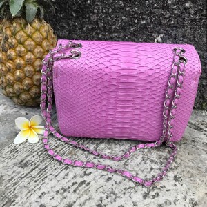 K&ouml;nnte beinhalten: Eine kleine, helllila Handtasche aus Schlangenleder mit einer silbernen Kettenkette.