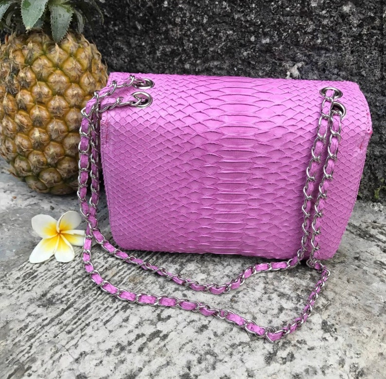 K&ouml;nnte beinhalten: Eine kleine, helllila Handtasche aus Schlangenleder mit einer silbernen Kettenkette.