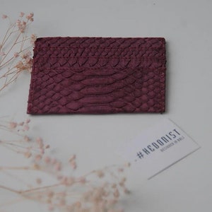 K&ouml;nnte beinhalten: Ein Kartenetui aus burgunderfarbenem Leder mit einem Schlangenhautpr&auml;gemuster. Das Kartenetui liegt auf einer wei&szlig;en Oberfl&auml;che mit einer Visitenkarte, auf der "#HEDONIST DESIGNED IN ITALY" steht.