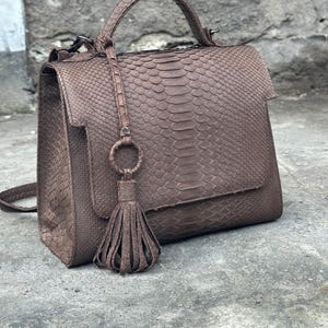 May include: A brown leather handbag with a snakeskin pattern and a tassel. The bag has a top handle and a shoulder strap.