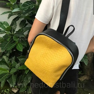 Könnte beinhalten: Ein gelber und schwarzer Lederrucksack mit Schlangenhautmuster. Der Rucksack hat einen Reißverschluss und verstellbare Träger.